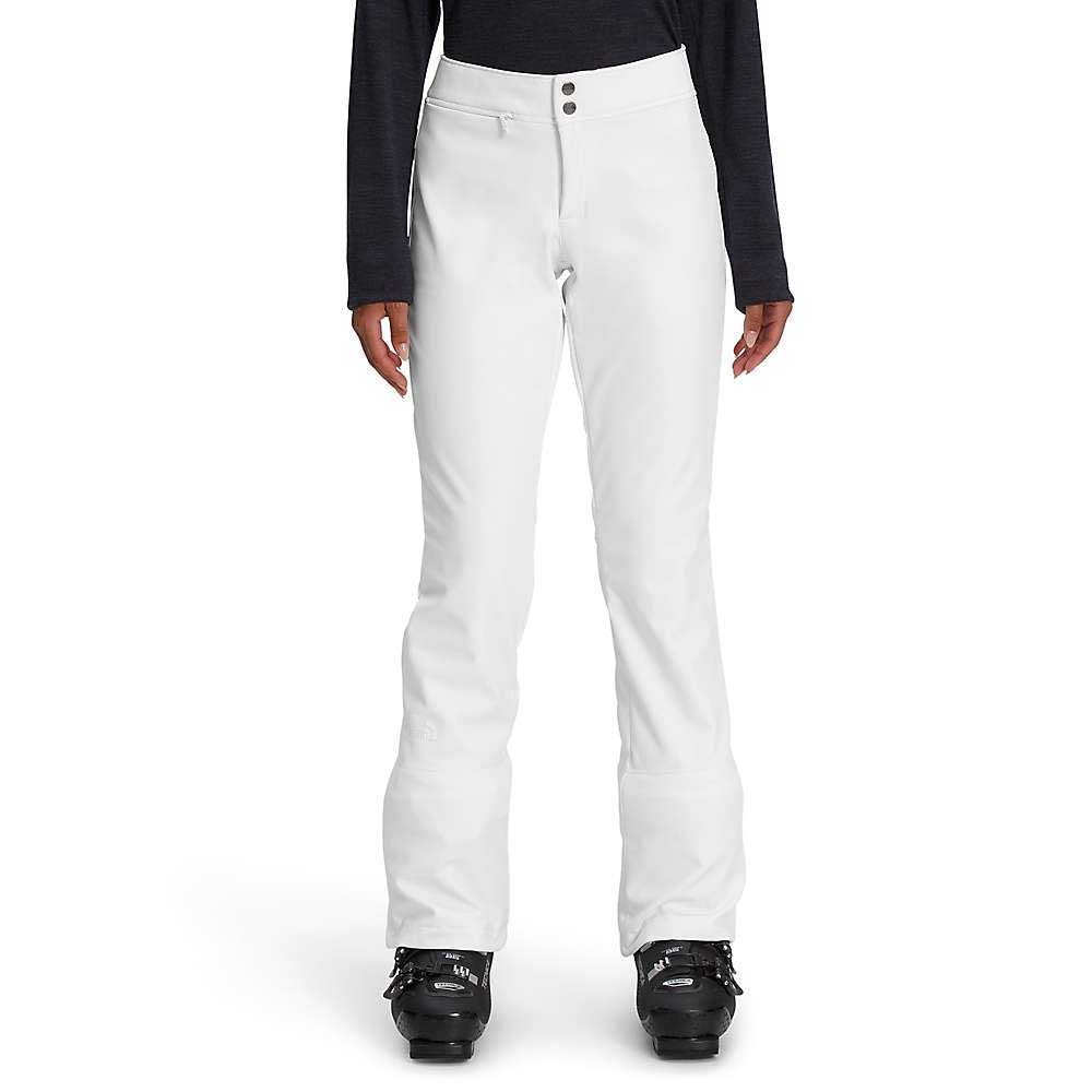 A person wearing The North Face Womens Apex STH Pant—windproof and water resistant—paired with a long-sleeve black top and black ski boots, stands upright against a plain white background.