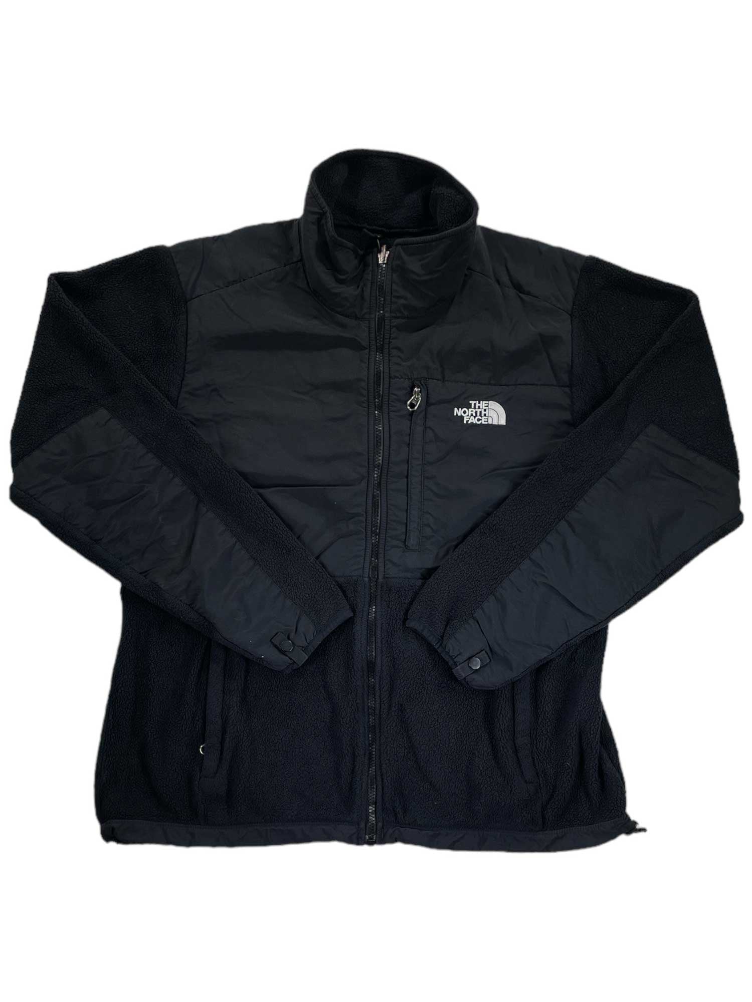The Denali Fleece Jacket by The North Face is black with a zip-up front, high collar, and logo on the left chest. Made from recycled fleece with smooth and textured panels, it offers zippered side/chest pockets for cold-weather comfort.
