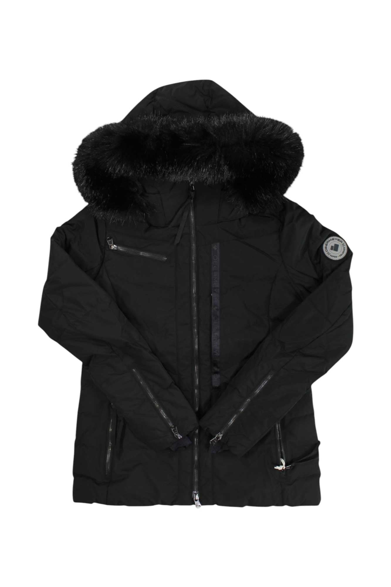 The Obermeyer Womens Circe Down Jacket is a black down jacket with a large fur-trimmed hood, front zipper, three zippered pockets, and a round upper-sleeve patch—ideal as a stylish winter sports jacket.