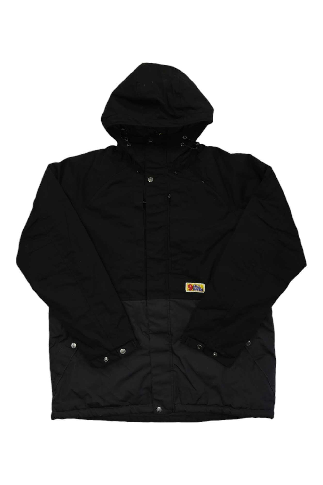 The Fjallraven Men's Vardag Lite Padded Jacket is black with a hood, snap buttons, front pockets, and a colorful patch. Made from G-1000 Eco fabric with recycled polyester insulation. Shown laid flat on a white background.
