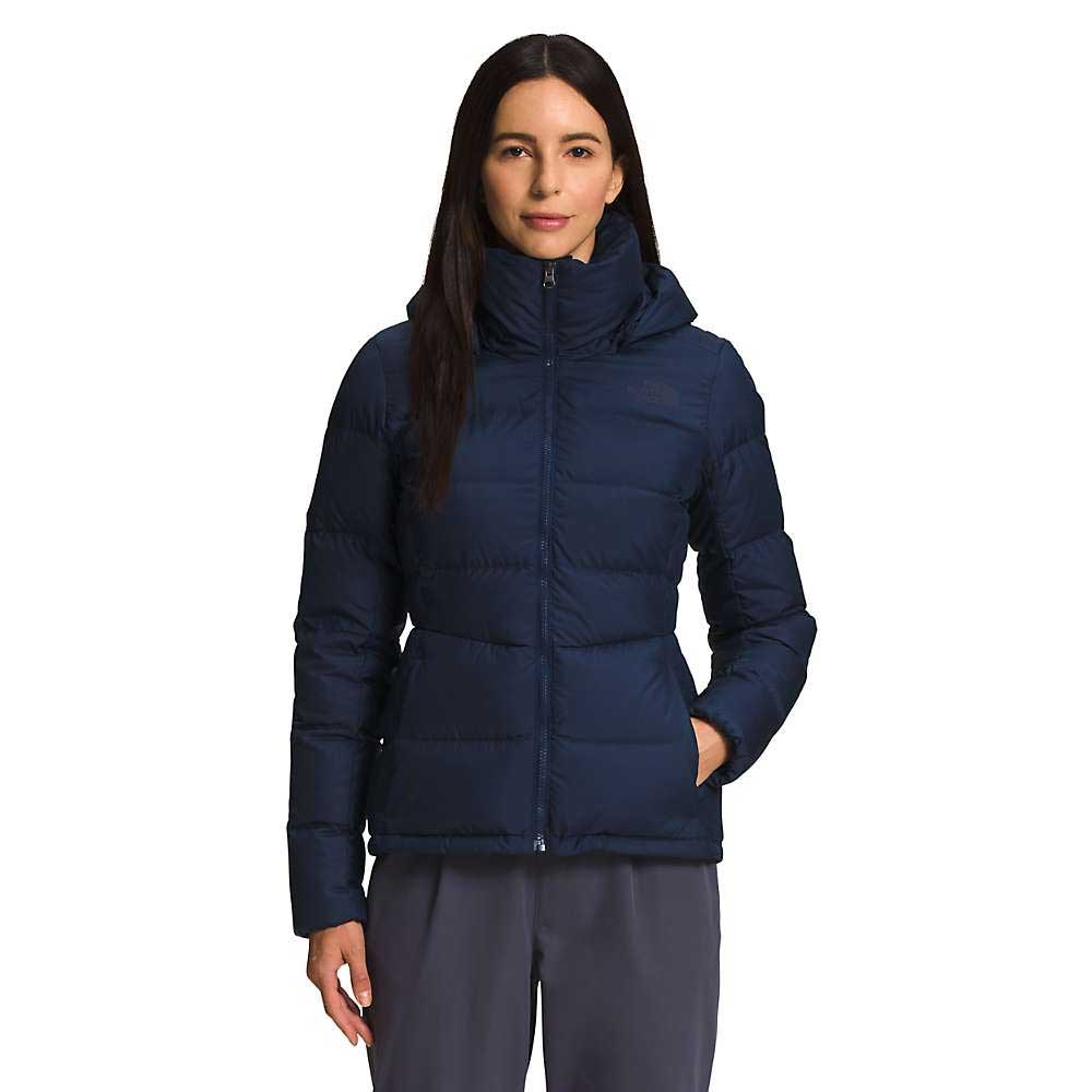 A woman with long dark hair wears a navy blue The North Face Womens Metropolis Jacket, standing facing forward with one hand in her pocket against a plain white background.