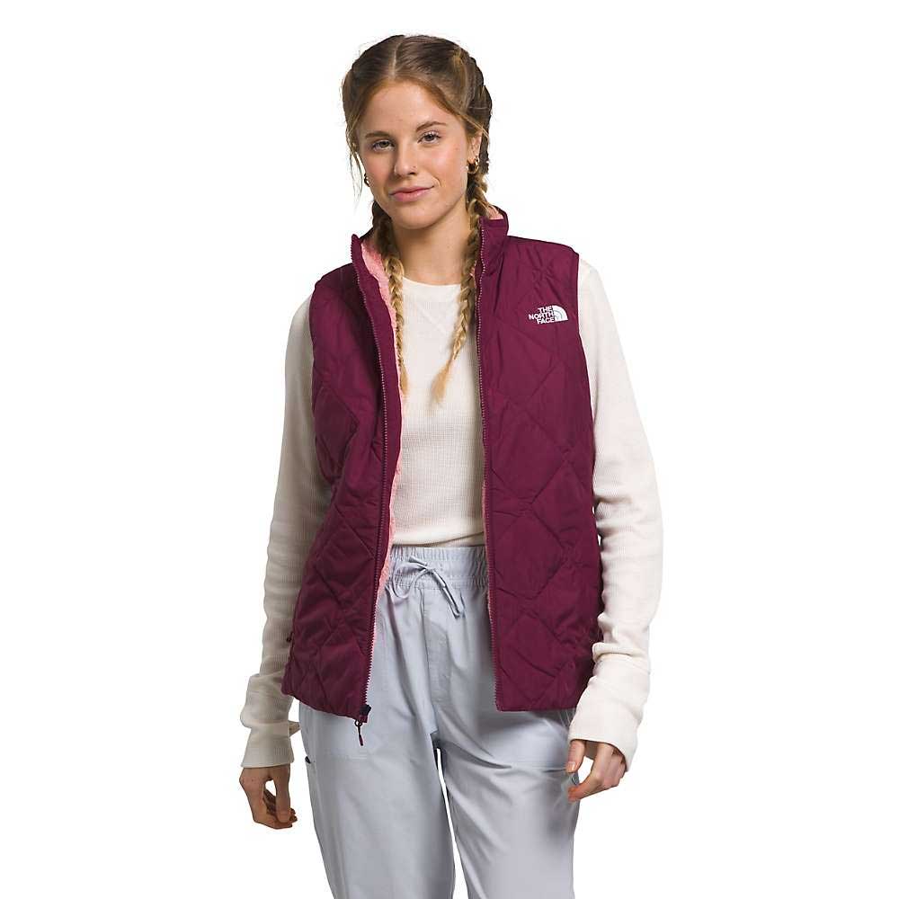 A young woman with braided hair wears The North Face Womens Shady Glade Insulated Vest, featuring recycled polyester and Heatseeker Eco insulation, over a white long-sleeve shirt and light gray pants against a plain white background.