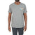 A man stands against a white background wearing the Moosejaw Mens Fearsome Critter SS Tee in heather gray, featuring a small moose and "W" graphic on the left chest, paired with dark pants.