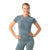 A woman stands smiling with her hands on her hips, wearing the Smartwool Womens Intraknit Active SS Top in a blue-gray leaf pattern and matching leggings, against a plain white background.