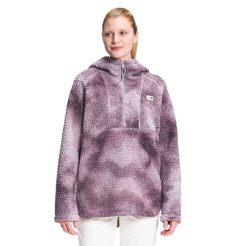 A woman wears The North Face Womens Printed Ridge Fleece Tunic in light purple, featuring a front zipper, textured eco-friendly Sherpa fabric, hood, and relaxed fit while posing with a slight smile against a plain white background.