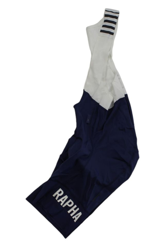 The Rapha Mens Pro Team Bib Shorts II - Regular features a dark blue lower, RAPHA in white, a white upper with black horizontal stripes on one strap, and a race-grade chamois for superior comfort.