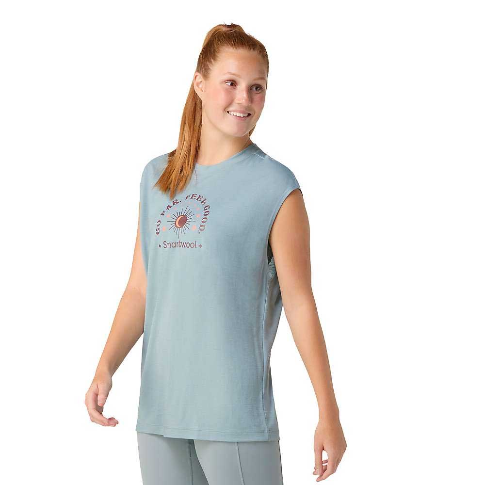 A smiling woman with long red hair in a ponytail wears a sleeveless light blue Smartwool Womens Active Muscle Tank and matching leggings, standing against a plain white background.