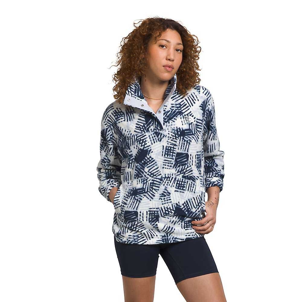 A person with curly hair models The North Face Womens Pali Pile Fleece 1/4 Snap—featuring blue and white abstract patterns—paired with black shorts, hands in pockets, standing against a plain white background.