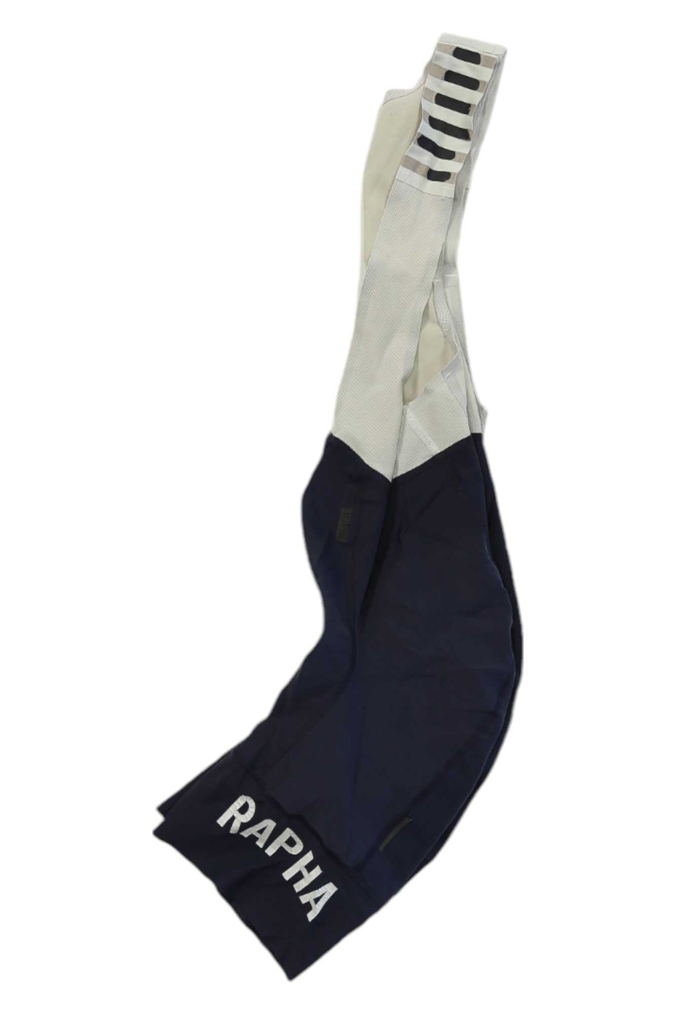 The Rapha Mens Pro Team Bib Shorts II - Regular features a navy blue and white design, white RAPHA text on one leg, black stripes on a shoulder strap, and a race-grade chamois for ultimate comfort.