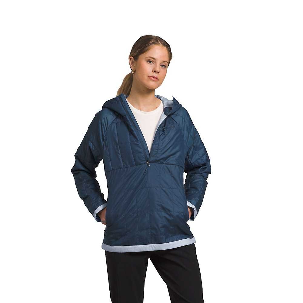 A woman stands against a white background wearing The North Face Womens Circaloft 1/4 Zip Pullover over a white shirt, hands in the pockets and a neutral expression on her face.