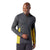 A man smiles while wearing the Smartwool Mens Merino Sport 150 LS 1/4 Zip Top—an athletic dark gray pullover with yellow accents on the sides and sleeves—as he looks down to his left.