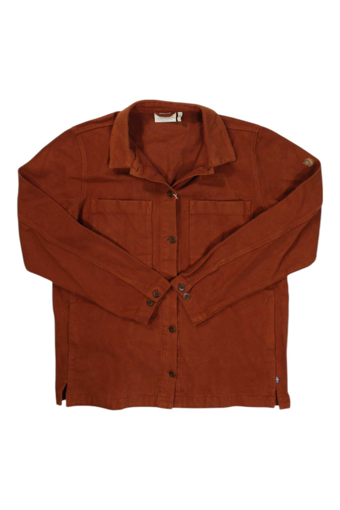 The Fjallraven Womens Singi Flannel Overshirt is a rust-colored, long-sleeve plaid shirt with two chest pockets, collar, and button cuffs, shown laid flat on a white background—ideal for layering as an outdoor overshirt.