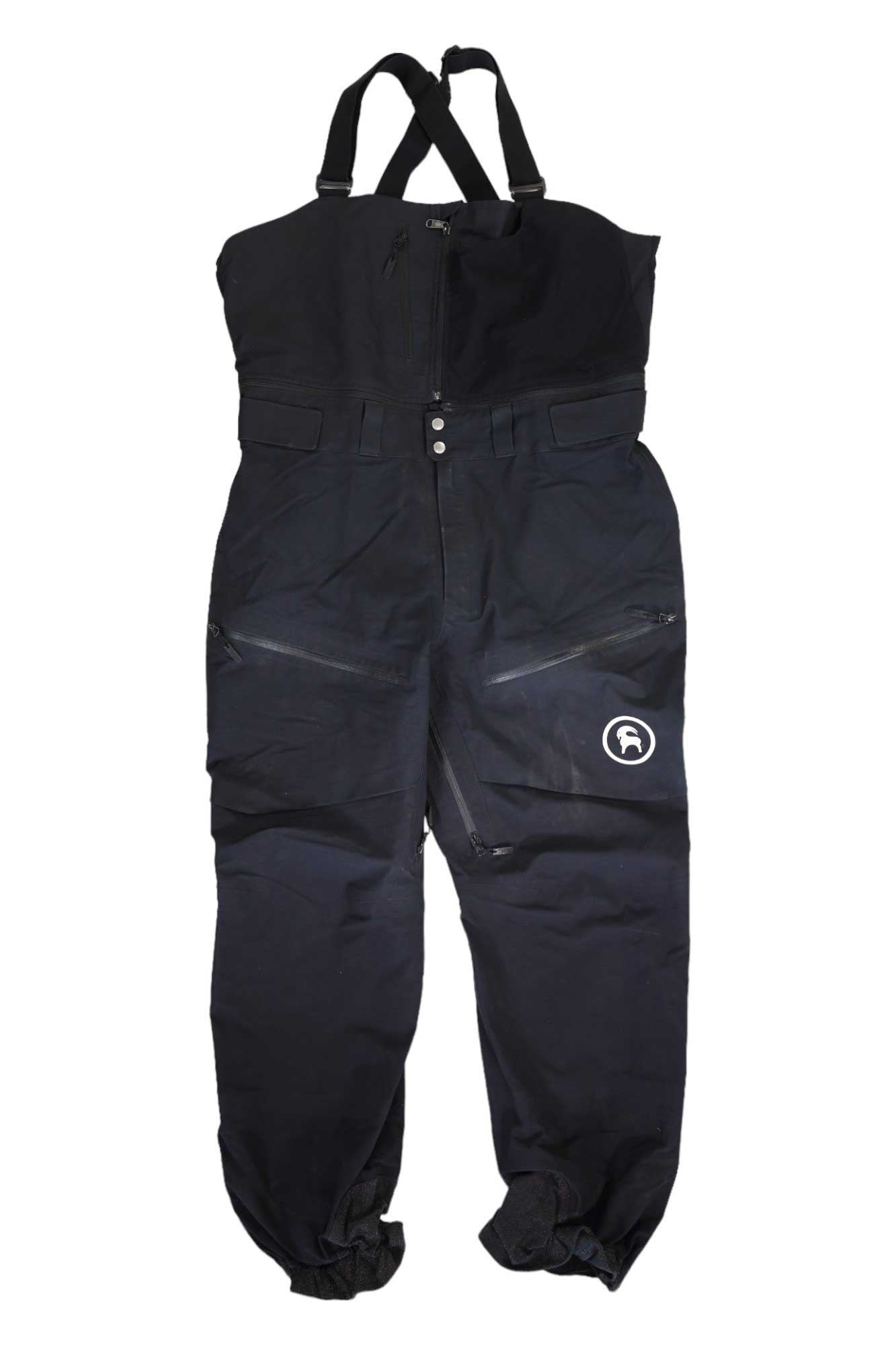 The Backcountry Cottonwood Bib Pant is black, waterproof, with adjustable suspenders, front zipper, two zippered thigh pockets, a white left leg logo, and elastic ankle cuffs—engineered for top backcountry performance.