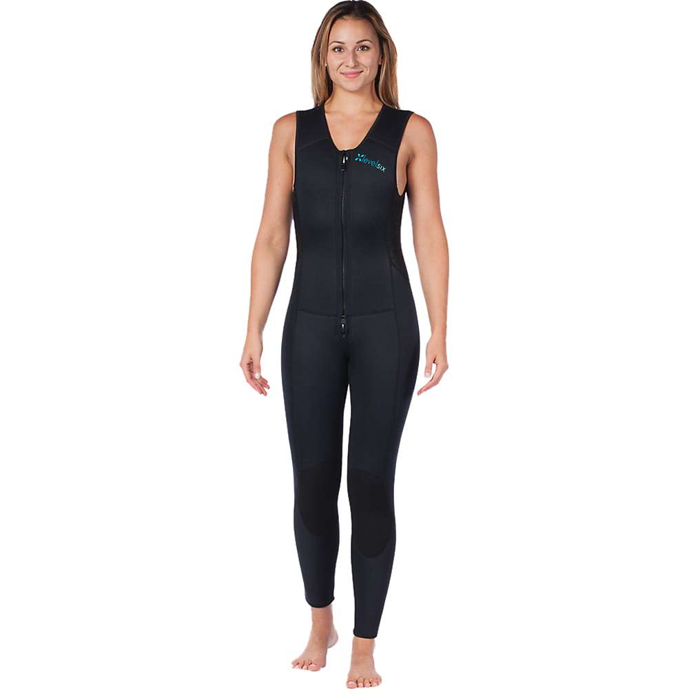 A woman stands barefoot, smiling, and wearing the Level Six Women's Farmer Jane Front Zip Wetsuit against a plain white background.
