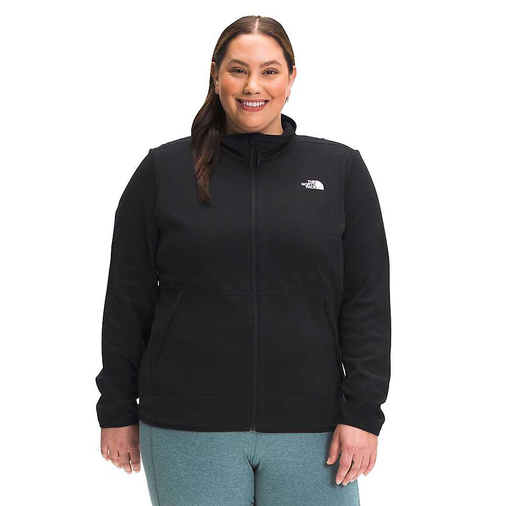 A woman with long brown hair in a ponytail smiles while wearing The North Face Womens Plus Canyonlands Full Zip Jacket in black and light blue pants, standing facing forward against a plain white background.