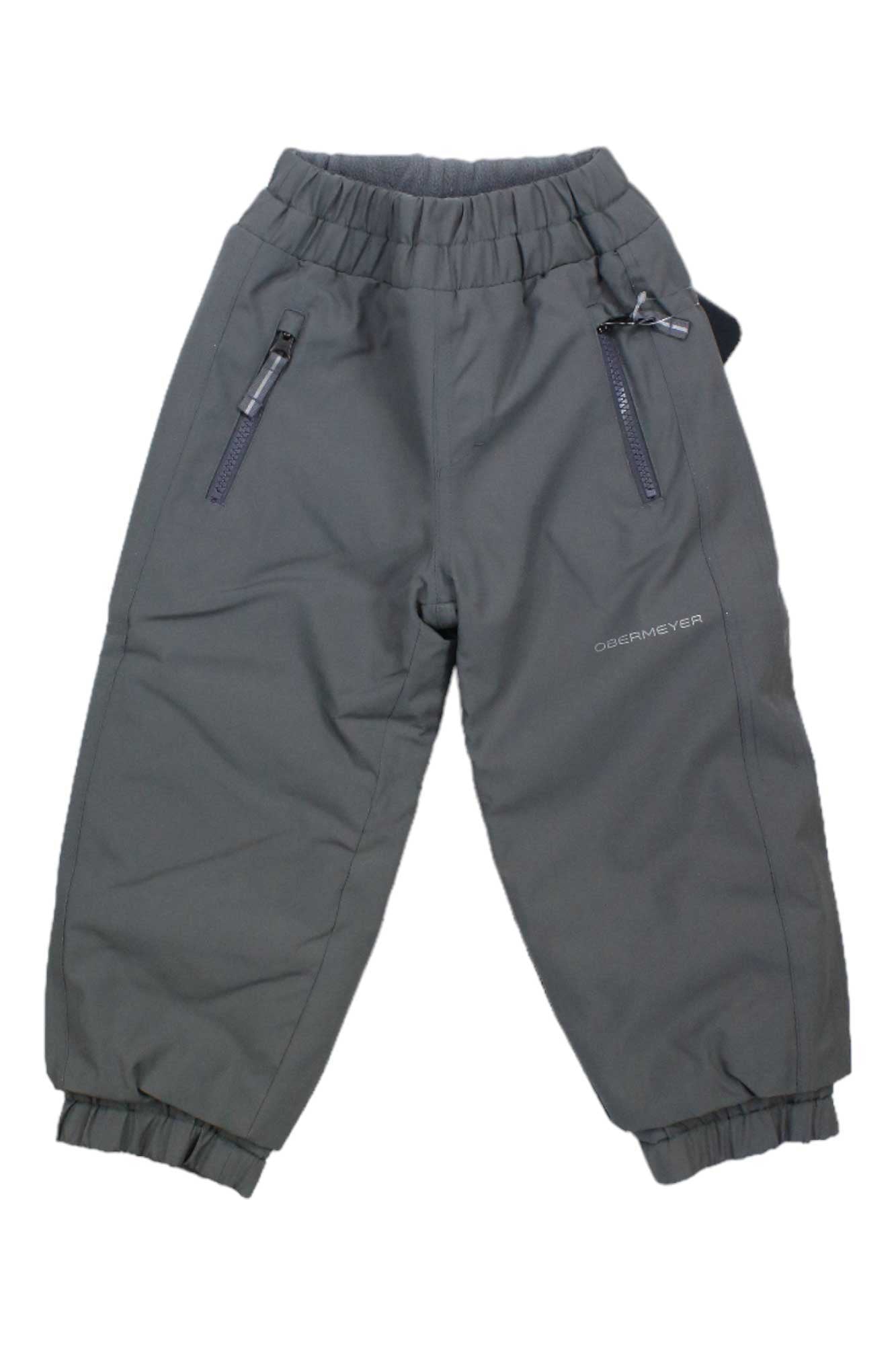 The Obermeyer Kids Campbell Pant is a pair of dark grey, insulated ski pants with elastic cuffs and waistband, two zippered front pockets, and the Obermeyer logo on the left leg.