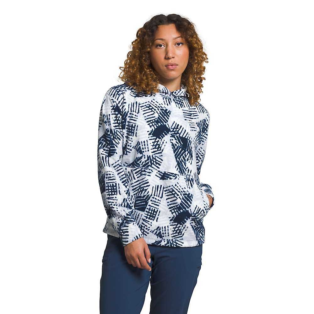 A person with curly hair wears The North Face Womens Pali Pile Fleece Hoodie in white with a navy geometric pattern and dark pants, standing with one hand in their pocket against a plain white background.