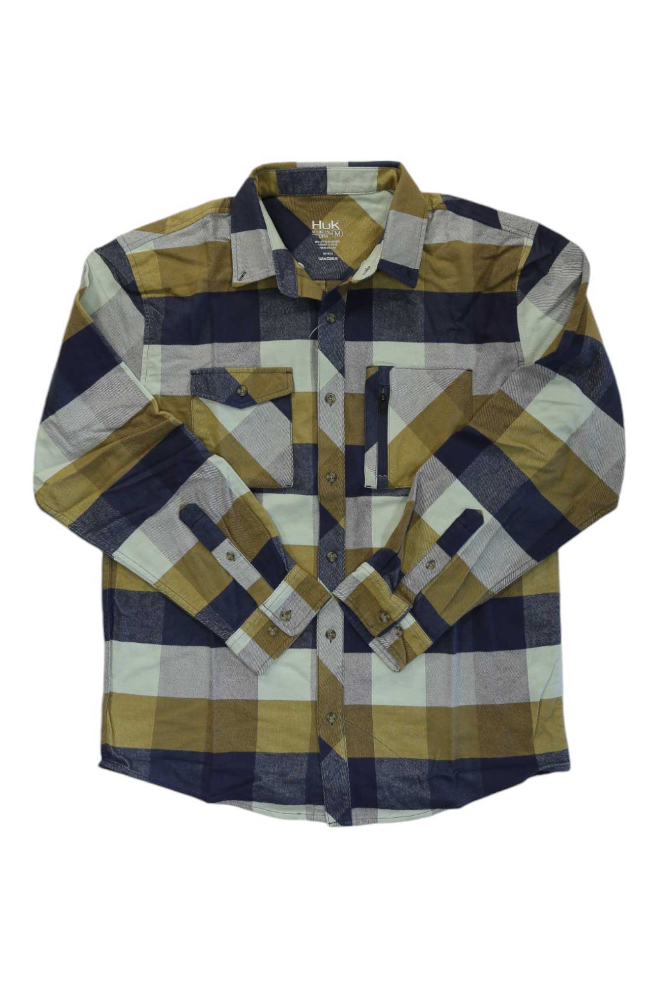 The Huk Men's Soft Stretch Flannel Shirt is a long-sleeve button-up with large navy, olive, tan, and white plaid, featuring two chest pockets including one with a zipper for added utility.