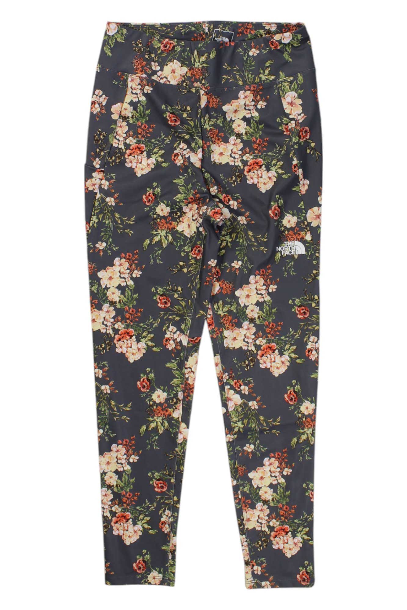 The North Face Girls' Printed On Mountain Tight leggings feature a vibrant floral print in pink, white, and red with green leaves, crafted from moisture-wicking fabric for comfort. Displayed flat on a white background.