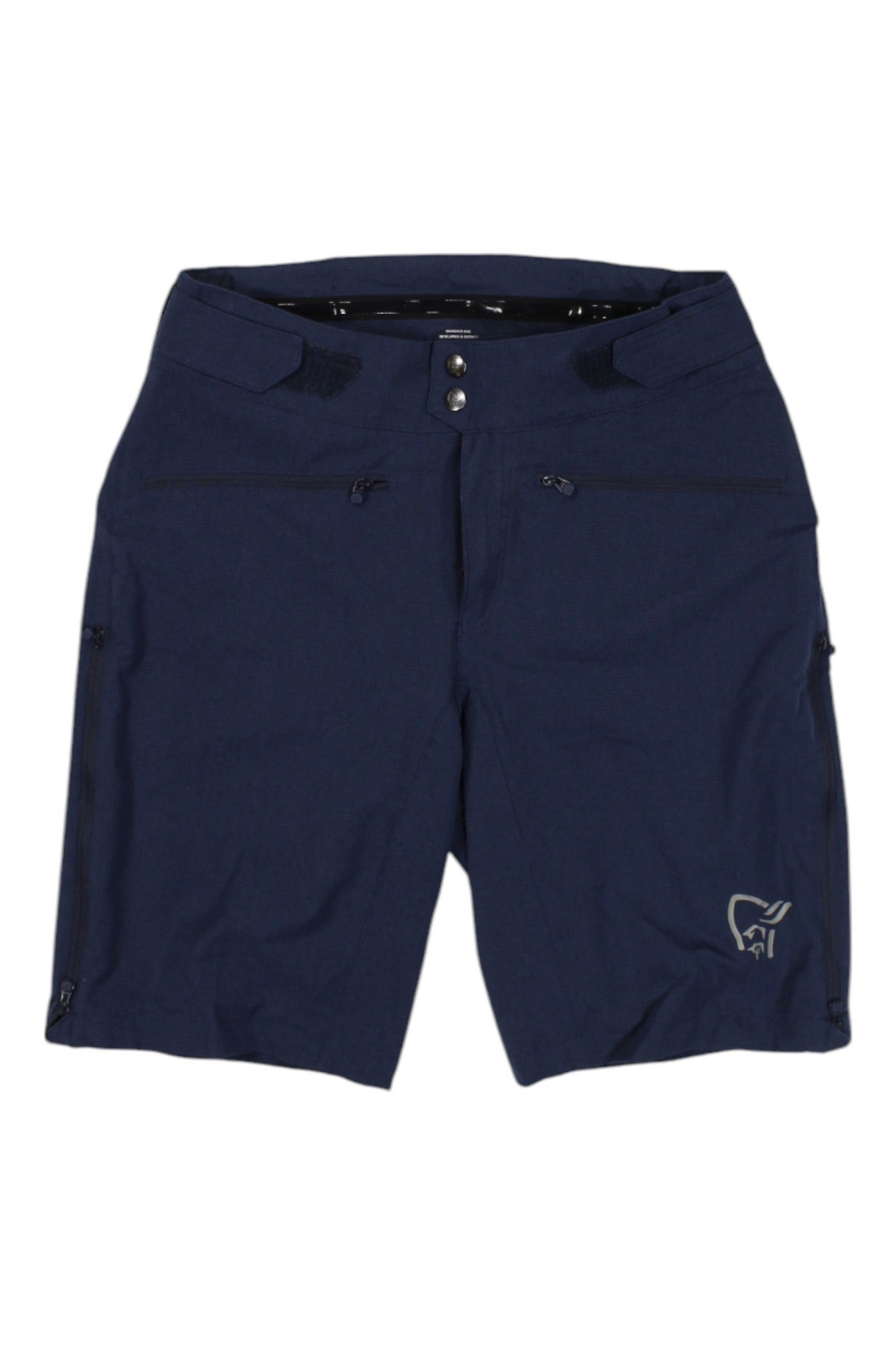 The Norrona Womens Fjora Flex1 Lightweight Short is a navy blue, knee-length mountain bike short with front zipper pockets, button and zip fly, small side zippers, and a subtle logo on the lower left leg.