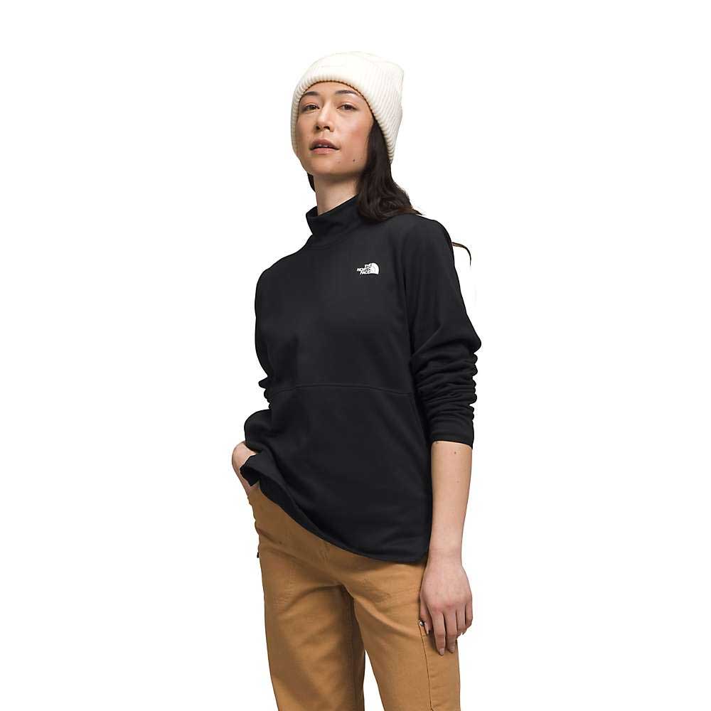 A woman wears a white beanie, tan pants, and The North Face Women's Canyonlands Pullover Tunic in black, standing with one hand in her pocket against a plain white background.
