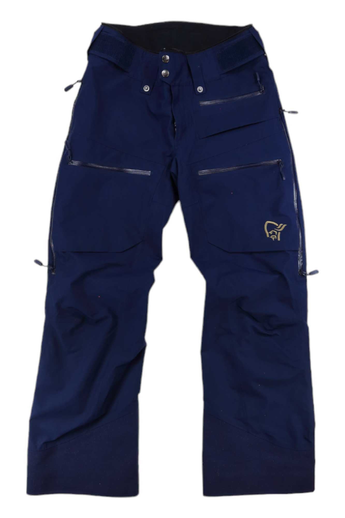 The Norrona Womens Lofoten GORE-TEX Insulated Snow Pants in navy blue feature multiple zippered pockets, reinforced knees, and a small yellow embroidered logo on the upper left thigh. They are displayed flat on a white background.