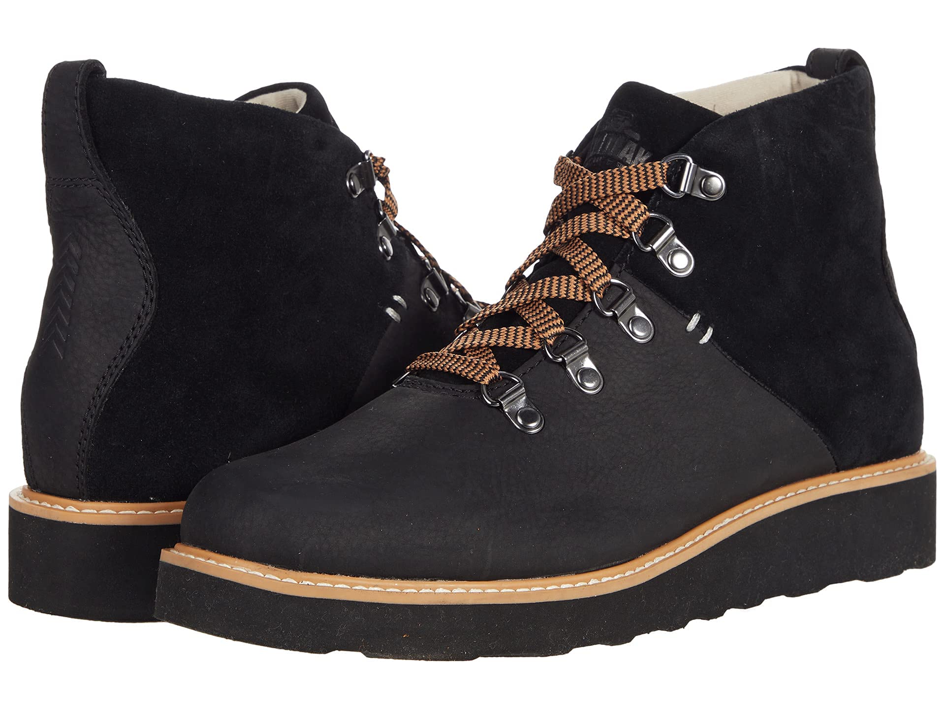 The Kodiak Sauveur Alpine Wedge Boot is a pair of black suede hiking boots featuring brown and orange striped laces, metal eyelets, tan stitching, thick black soles, and displayed in both side and front views.