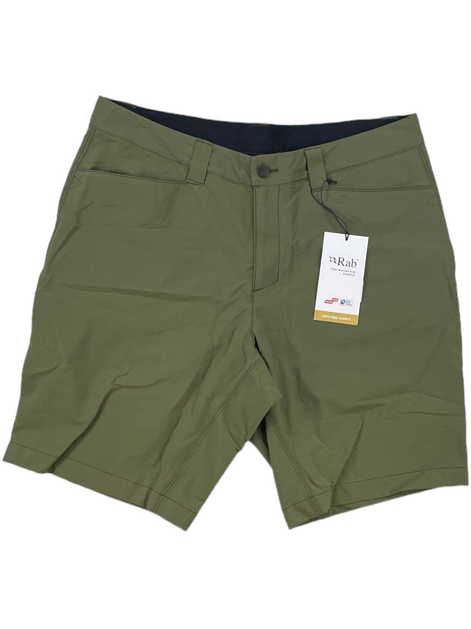 The Rab Mens Capstone 10 Inch Short in olive green features a button closure, front pockets, moisture-wicking fabric, and a white Rab tag by the waistband. Shown laid flat on a white background.