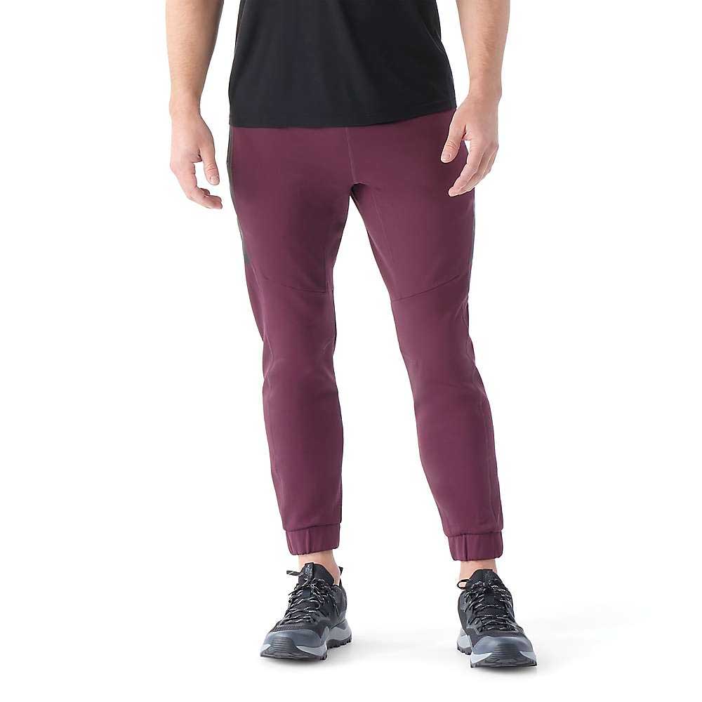 A person wearing a black T-shirt, Smartwool Men's Active Fleece Tech Pant in maroon, and black athletic shoes stands against a white background. The image captures the person from shoulders to feet.