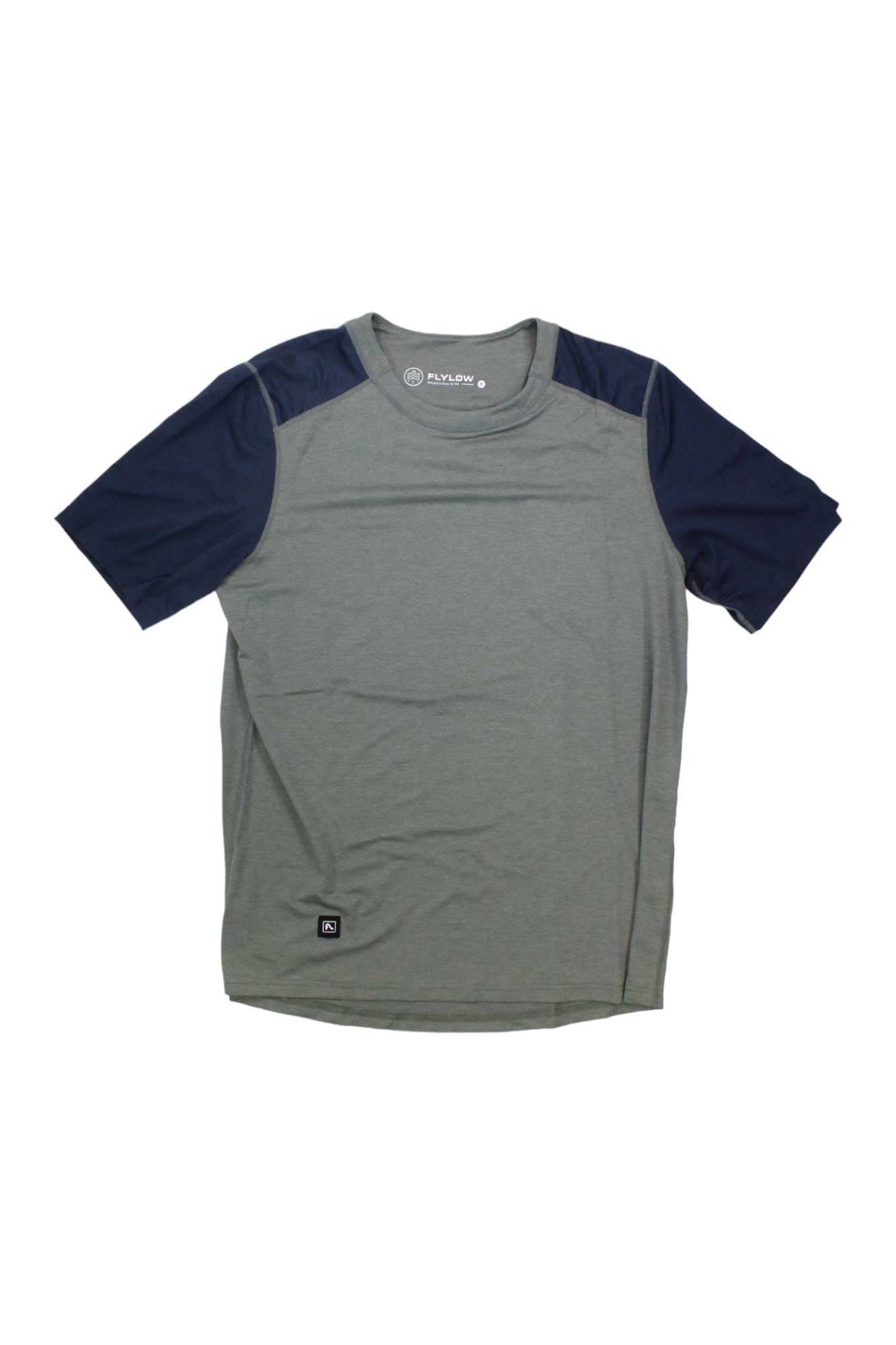 The Flylow Mens Garrett Shirt is a short-sleeve performance top with a gray body and dark navy sleeves and shoulder panels, shown against a plain white background.