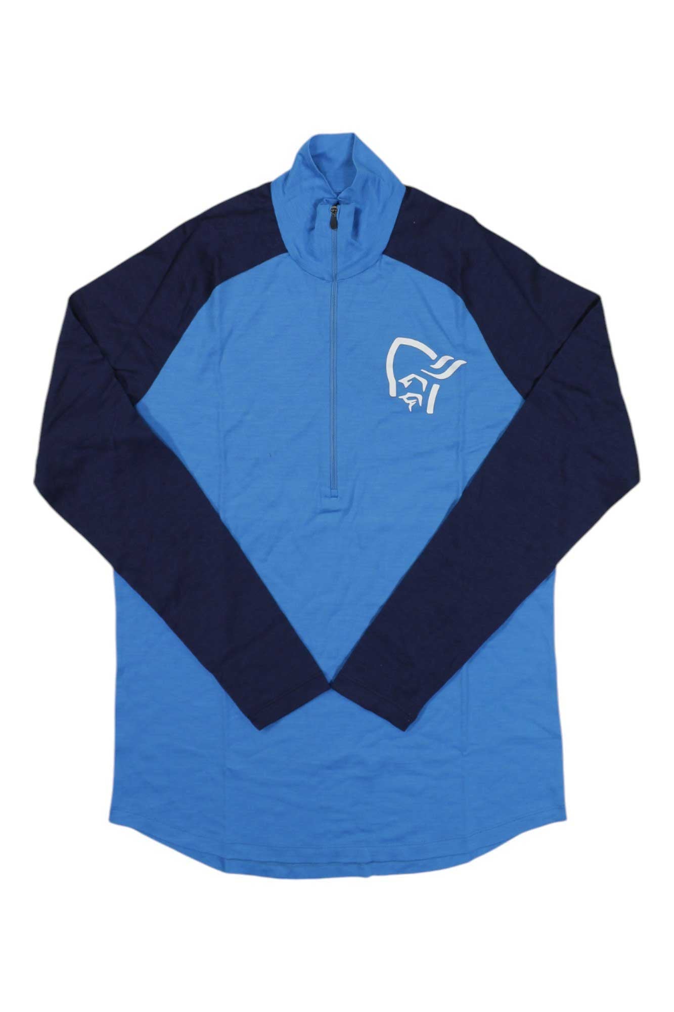 The Norrona Mens Pureull Zip Neck Top is a moisture-wicking long-sleeve with a light blue body, dark blue sleeves and shoulders, and a white graphic logo on the left chest.