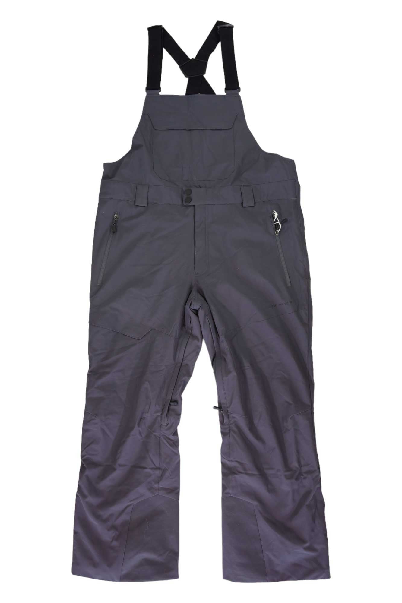 Obermeyer Mens Perseus Bib Pant in dark gray, featuring adjustable black straps, chest pocket, front button and zipper closure, plus two zippered side pockets—insulated and waterproof ski bib overalls for snowsports.