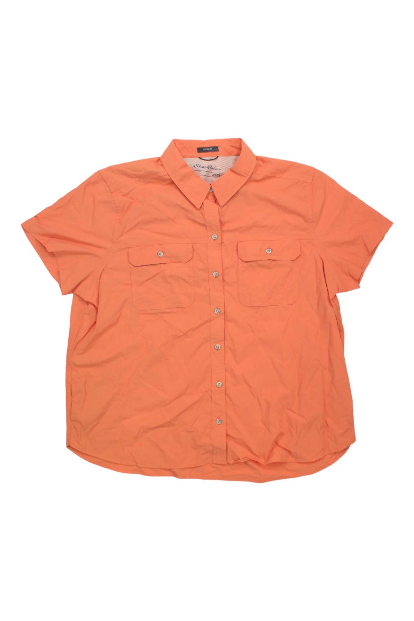 The Eddie Bauer Travex Women's Mountain 2.0 SS Shirt is a light orange, short-sleeved, button-up top with two chest pockets, a collar, and UV protection—shown laid flat on a white background.
