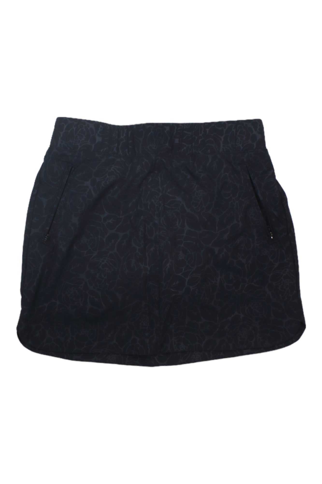 The Embossed Pull On Travel Skort is a black mini skort with subtle floral embossing, front zipper pockets, and an elastic back waistband for comfort.