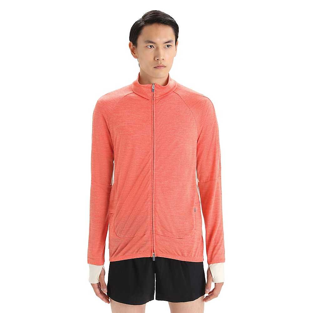 A person with short dark hair wears the Icebreaker Mens ZoneKnit LS Zip Jacket in coral with long sleeves and black shorts, standing against a white background.