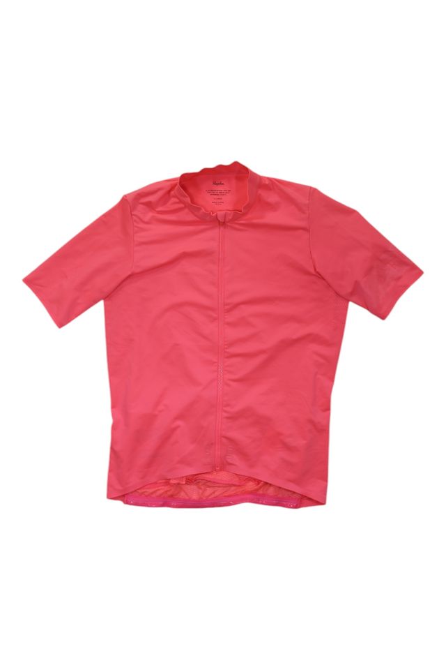 The Mens Pro Team Midweight Short Sleeve Jersey in bright pink features a front zipper and high collar. Designed for men, this Rapha jersey is ideal for comfortable rides in changing conditions and is shown laid flat on a white background.