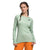 A woman with braided hair wears The North Face Womens Fd Pro 160 Crew in light green, made from recycled polyester, paired with orange pants, standing with one hand on her hip against a white background.