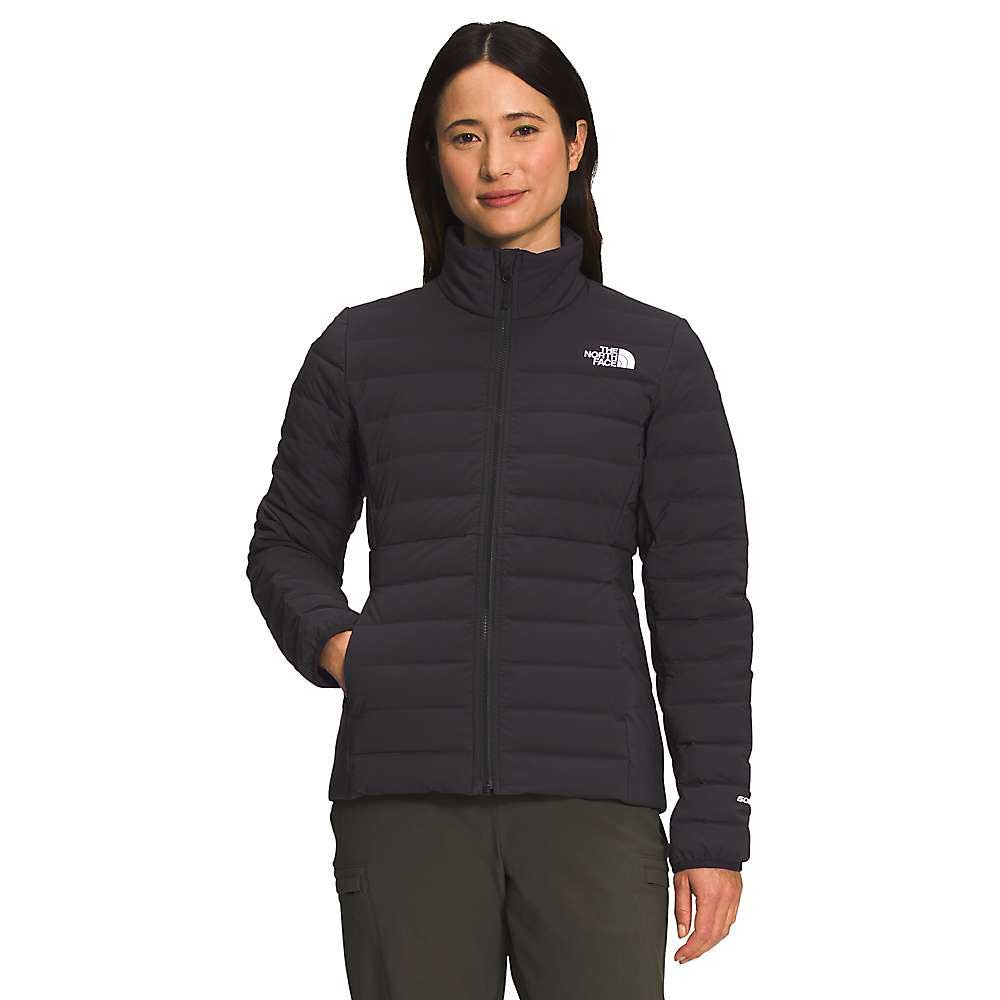 A woman stands facing forward with hands in pockets, wearing The North Face Women's Belleview Stretch Down Jacket in black and water-repellent fabric, against a plain white background.