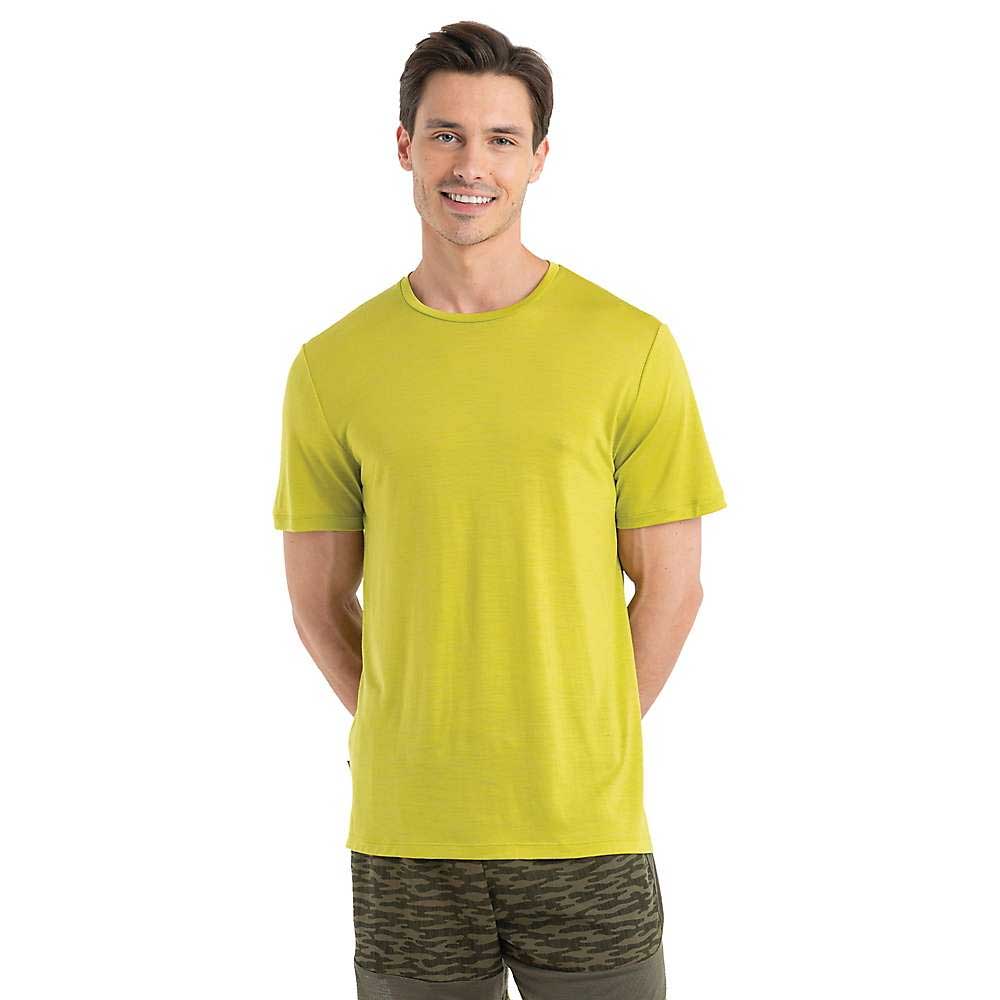 A man with short brown hair, wearing the Icebreaker Mens Sphere II SS Tee in bright yellow-green and olive green camouflage shorts, stands facing forward and smiles at the camera against a white background, ready for hiking adventures.