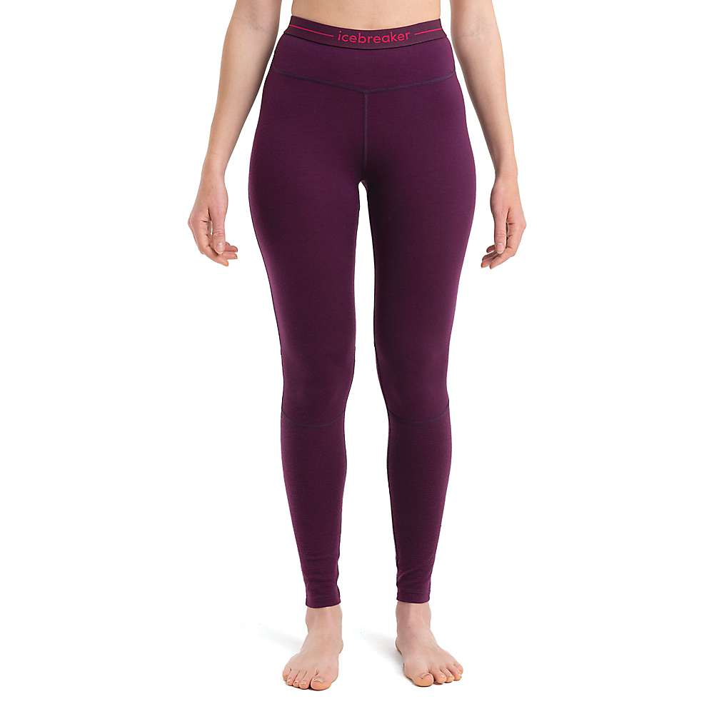 A person stands barefoot wearing high-waisted Icebreaker Womens 200 Zoneknit Merino Wool leggings in purple, with "icebreaker" on the waistband. Photo is cropped from shoulders down against a white background.