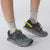 A person wearing light beige Salomon socks and gray Salomon Predict Hike GTX Shoes - Turquoise, with aqua and yellow accents, standing on a white background.