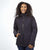 A woman with curly hair smiles while wearing the Moosejaw Women's Hooded Insulated Jacket in black, featuring synthetic insulation and weather resistance, with her left hand in the pocket against a plain white background.