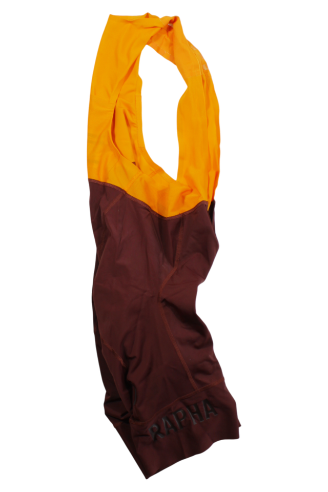 A crumpled Rapha Mens Pro Team Bib Shorts II - Regular cycling jersey with an orange top half and maroon bottom half, featuring "RAPHA" in black on the lower section—perfectly matching your favorite bib shorts.