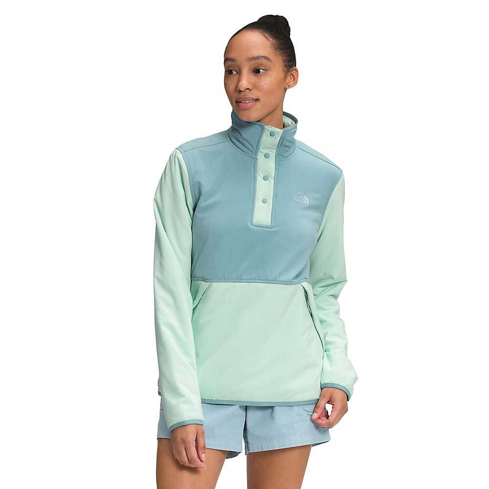 A woman wears the Women's Mountain Sweatshirt Pullover 3.0 in light blue and mint green, featuring a high collar and snap buttons, made from recycled polyester. She pairs it with matching shorts and smiles gently while looking to the side.