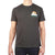 A person wears the Moosejaw Men's Cream Cheese SS Tee, a dark gray short-sleeve shirt with a small mountain and sun graphic plus "Moosejaw" on the left chest. The person's head is not shown in the photo.
