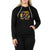A woman wears the Moosejaw Women's Granola Pullover Hoody, a black recycled polyester fleece hoodie with camping graphics and "Moosejaw" on the front, standing with one hand in the pocket against a white background.
