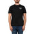 A man wearing the Moosejaw Mens Fearsome Critter SS Tee, a black casual shirt with a white graphic logo on the left chest, paired with blue jeans and standing against a plain white background.