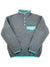 The Women’s Lightweight Synchilla Snap-T Fleece Pullover is a gray polyester fleece with light blue-green trim, high collar, long sleeves, chest pocket, and visible Patagonia logo. Fair Trade Certified.