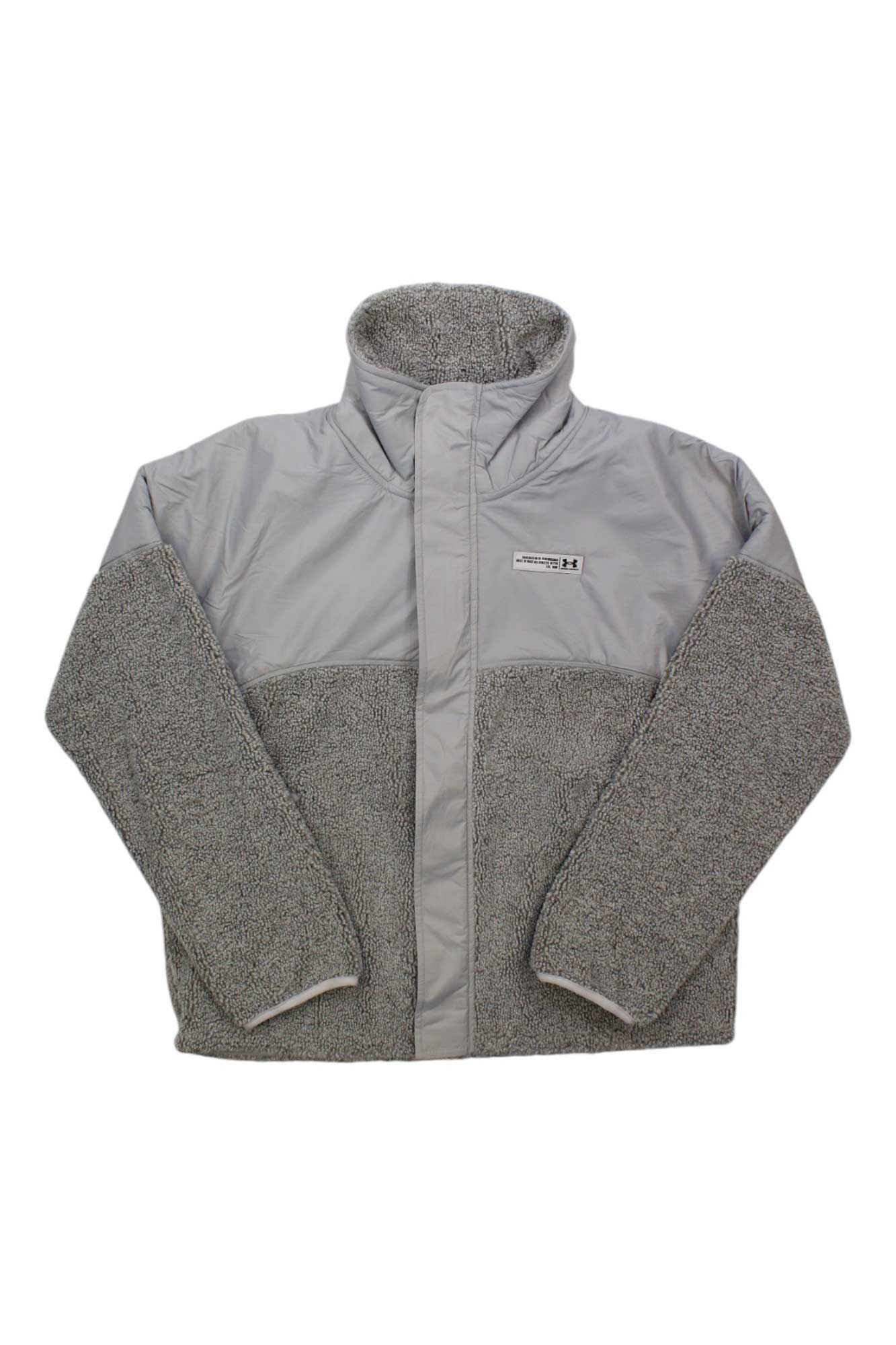 The Under Armour Womens Mission Boucle Swacket is a light gray zip-up jacket with a high collar, featuring smooth fabric on the top half and fuzzy boucle material on the sleeves and lower half.