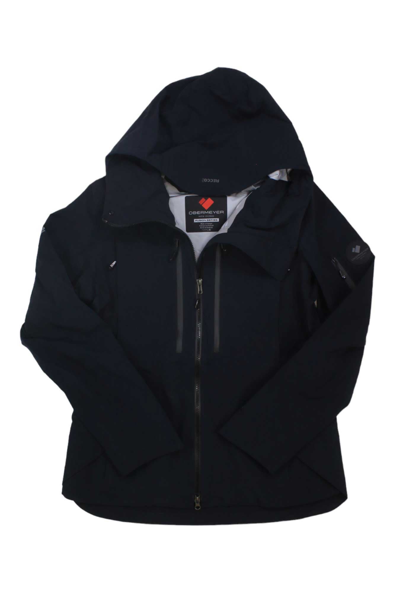 The Obermeyer Womens Highlands Shell Jacket is black, weather-resistant, features a front zipper, two zippered chest pockets, and a visible collar tag. The jacket is shown laid flat with sleeves crossed at the cuffs.